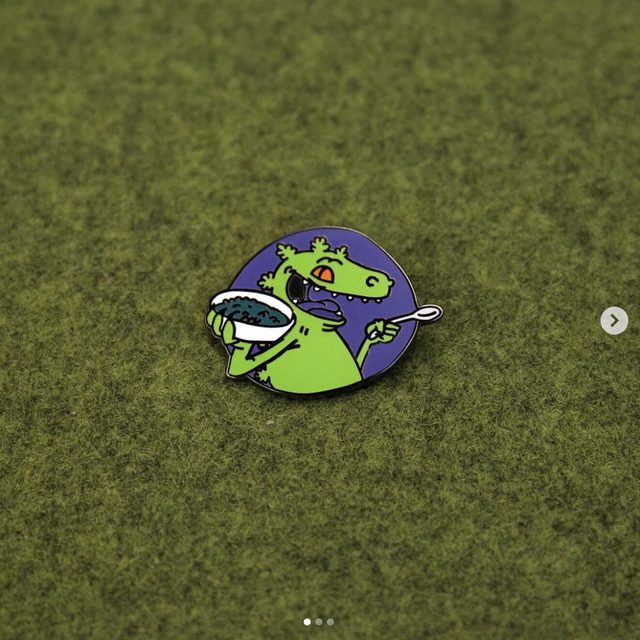 Custom Reptar cereal enamel pin on a green background